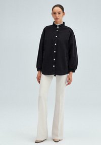 Zwarte denim oversized shirtjack met een hoge kraag, voor sluitingen met knopen en zijzakken, gecombineerd met lichtgekleurde flared broeken.