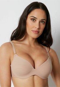 Beige padded bra with an underwire design, smooth texture, and adjustable straps featuring gold-toned hardware.
