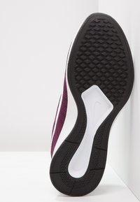 Nike-tenniskenkä, jossa on violetti yläosa, valkoiset yksityiskohdat ja teksturoitu musta kumipohja, jossa on kuusikulmainen kuvio pidon parantamiseksi.