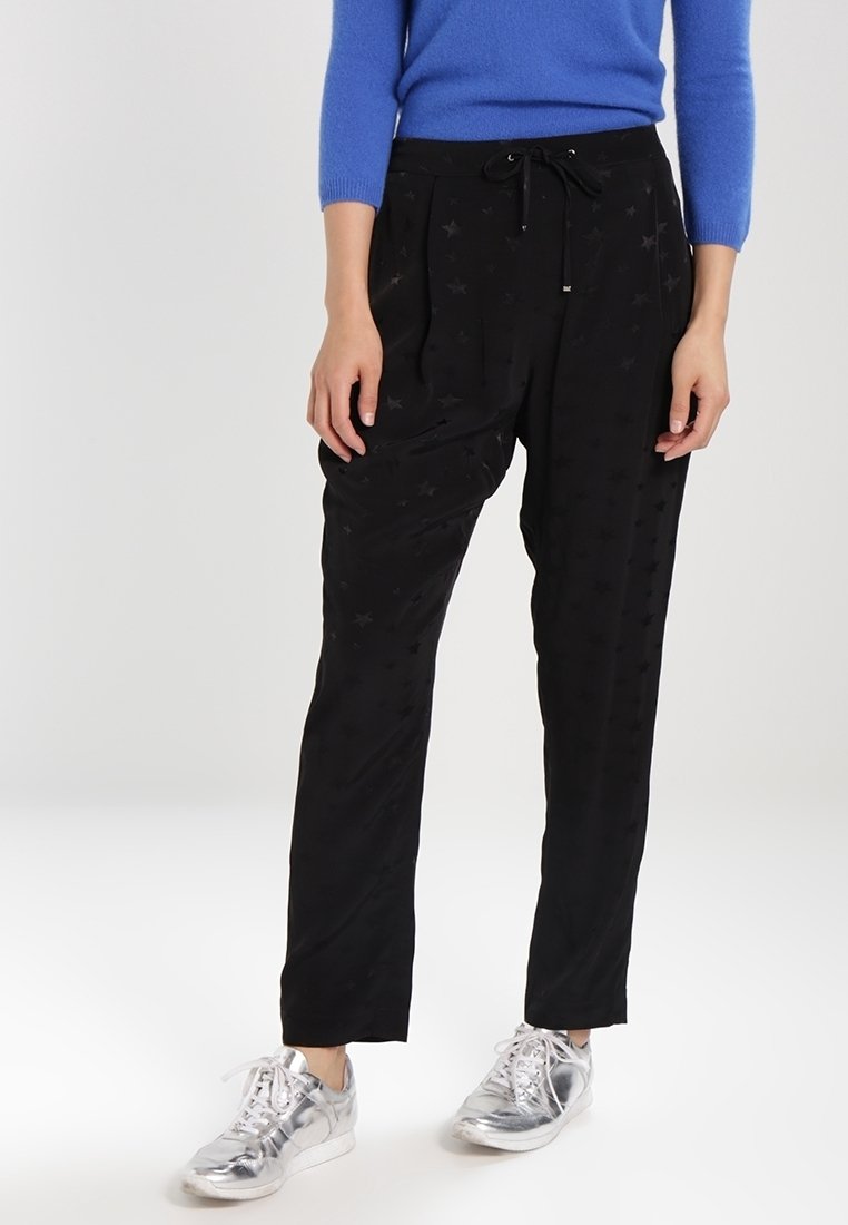 Svarta byxor med stjärnmönster, med dragsko i midjan, snäva ben och en slät textur. Bärs med silverfärgade sneakers och en blå tröja.