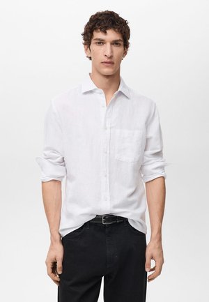 White long-sleeve shirt in linen fabric with a button-down collar and a single pocket; paired with black pants and a black belt.