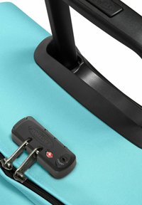 Maleta de tela azul con textura, con asa retráctil negra y cerradura negra que incluye un indicador de seguridad. Cierres de cremallera visibles.