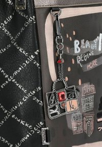 Schwarze Handtasche aus strukturiertem Leder, mit silbernem Zubehör und einem Charme in Form einer Tasche mit einem roten Edelstein. Die Muster enthalten handgeschriebenen Text.