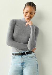 Grau gerippter Rollkragen-Pullover mit langen Ärmeln, kombiniert mit hellblauen, hoch taillierten Jeans und einem schwarzen Gürtel mit goldener Schnalle.