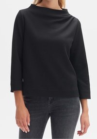 Maglione nero in tessuto texturizzato, con scollatura a barca, maniche tre quarti e orlo dritto, abbinato a jeans grigio scuro.