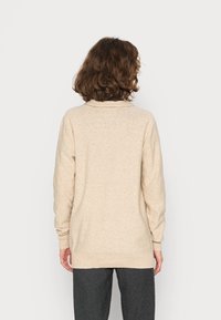 Beżowy sweter z dzianiny z kołnierzem, długimi rękawami, luźnym krojem i prążkowanym dołem; gładka faktura, bez widocznych wzorów ani elementów metalowych.