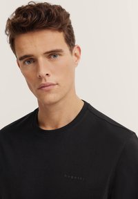 Czarny bawełniany T-shirt z okrągłym dekoltem i krótkimi rękawami. Z przodu znajduje się subtelne logo marki. Miękka tekstura.