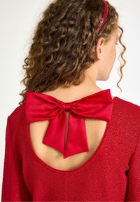 Rotes Kleid mit schimmernder Textur, featuring eine große, satinierte Schleife hinten und einem abgerundeten Ausschnitt unterhalb des Kragens.