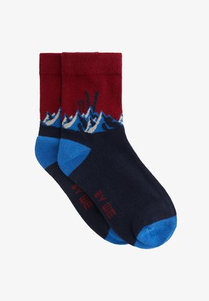 Sokker med en rød overdel med blå accenter, mørkeblå krop og et bølgemønster i blå og hvid. Tekst trykt i rødt på tåen.