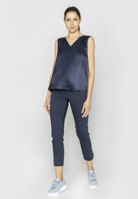 Niebieska satynowa bluzka bez rękawów z dekoltem w serek, zestawiona z dopasowanymi granatowymi spodniami i jasnoniebieskimi trampkami, które mają dekoracyjne akcenty.