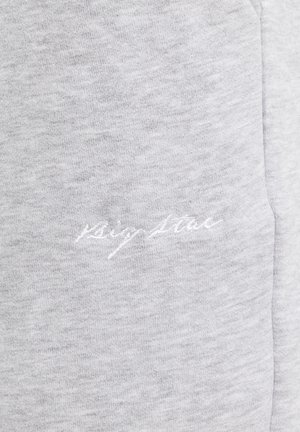 Tela gris claro con sutil bordado blanco en cursiva que dice "Sign Stone" cerca de una costura.