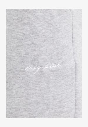 Hellgrauer Stoff mit subtiler weißer kursive Stickerei mit der Aufschrift "Sign Stone" nahe einer Naht.