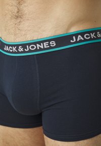 Marineblaue Baumwoll-Boxershorts mit einem kontrastierenden türkis-weißen Bund, auf dem "JACK & JONES" mehrfach gedruckt ist.