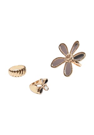 Tre guldringe, to med blomstermotiver—en stor med grå kronblade, en mindre med sorte kronblade—og en ribbet, ensfarvet ring på hvid baggrund.