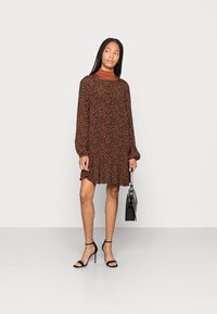 Vestido de estampado animal em tons de castanho com mangas longas e saia franzida. Combinado com sandálias pretas e uma mala estruturada para criar contraste.