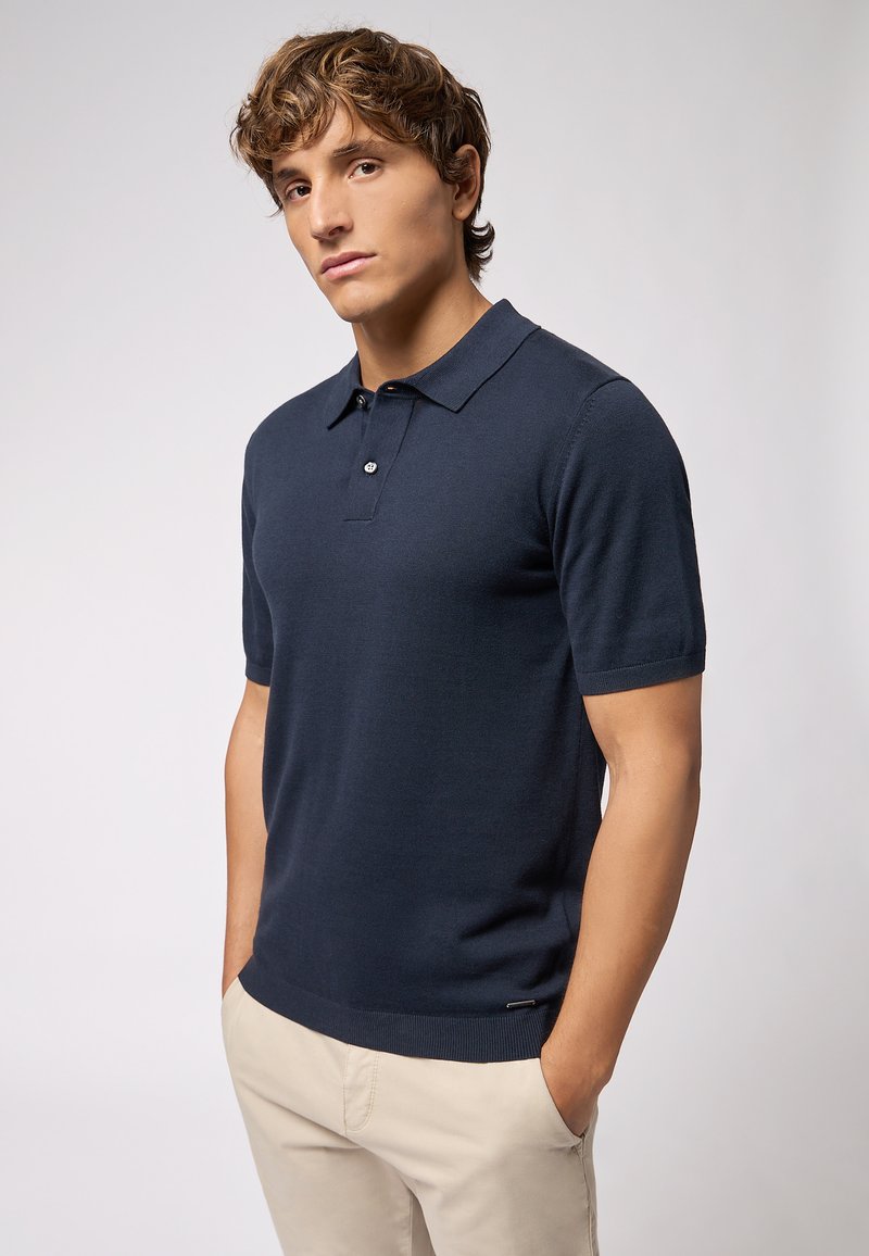 Navy blue short-sleeve polo shirt made from a smooth knit material, featuring a pointed collar and subtle logo detail at the hem.