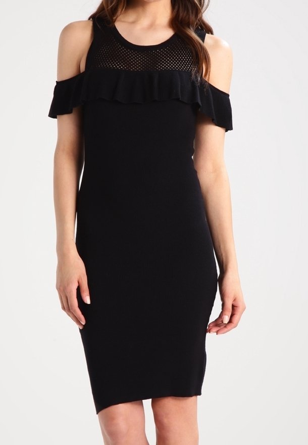 Robe noire à épaules dénudées avec détail volanté et empiècement en résille au niveau de l'encolure, portée par une femme debout.