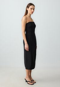 Abito midi nero senza spalline con texture a coste, silhouette aderente e spacchi laterali. Abbinato a sandali flip-flop neri.