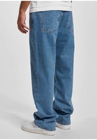 Jeans de mezclilla azul con un corte amplio, que presentan dos bolsillos traseros, una silueta de pierna recta y un acabado liso, ligeramente texturizado.