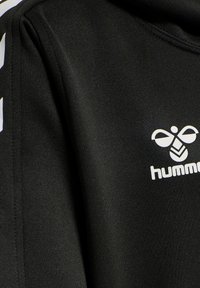 Schwarzer Pullover mit glatter Textur, ausgestattet mit einem weißen Logo und Designakzenten entlang des Ärmels. Einfacher, moderner Schnitt.