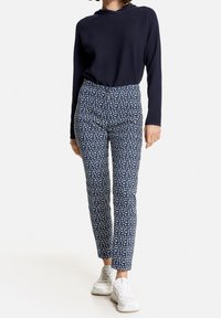 Pull marin à capuche, assorti à un pantalon ajusté avec un motif blanc sur fond bleu marine ; le modèle porte des baskets blanches.