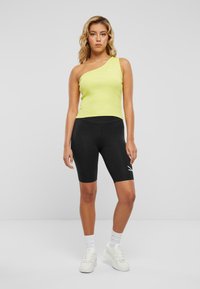 En-skulder limegrønn ribbet tanktopp kombinert med svarte sykkelshorts. Hvit logo detalj på shortsene og hvite sneakers med ankelsokker.