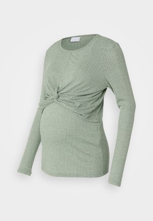 Top per maternità in tessuto a coste verde chiaro, con maniche lunghe e un design annodato sul davanti, progettato per una pancia in crescita.