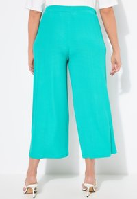 Pantaloni ampi turchesi in tessuto a costine, con vita elasticizzata e lunghezza cropped, abbinati a sandali bianchi con tacco.