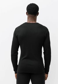 Čierne termo tričko s dlhým rukávom s rebrovanou textúrou, priliehavým strihom a okrúhlym výstrihom, doplnené o čierne nohavice v rovnakom dizajne.