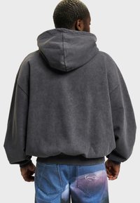 Overdimensioneret sweatshirt i mørkegrå bomuldsblanding med en struktureret overflade, der har en stor hætte og ribbet kant, båret med multifarvet denim.