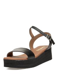 Sandalias cuña negras con un upper texturizado y una plantilla marrón lisa. Cuenta con una correa ajustable en el tobillo y una suela apilada y estriada.