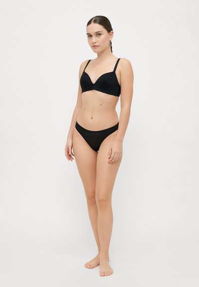 Bralette de encaje negro con aros, escote pronunciado y tirantes ajustables. Bikini de talle bajo a juego con lados finos y textura sutil.