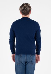 Granatowy sweter wykonany z miękkiego materiału dzianinowego, z okrągłym dekoltem, długimi rękawami i dopasowanym dołem. Nosi się go z niebieskimi dżinsami.