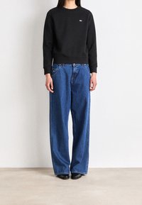 Svart sweatshirt med rund halsringning, i kombination med lösa blå denimjeans. Jeansen har en klassisk femfickdesign. Svarta skor fulländar outfiten.