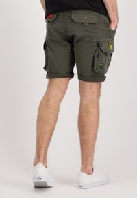Olive green cargo shorts with rolled cuffs, featuring multiple pockets and patches. Pairing with white sneakers for a casual look.