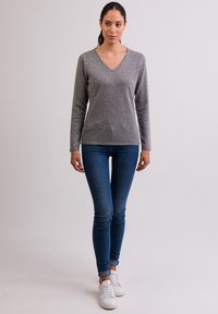 Maglione grigio a V in tessuto morbido, maniche lunghe, design aderente, abbinato a jeans blu e sneakers bianche. Look minimalista e casual.