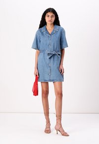 Denim kleita ar īsām piedurknēm, pogu aizdare priekšā, josta viduklī, gaiši zilā krāsā. Stilizēta ar beigo siksniņu papēžiem un sarkanu maku.
