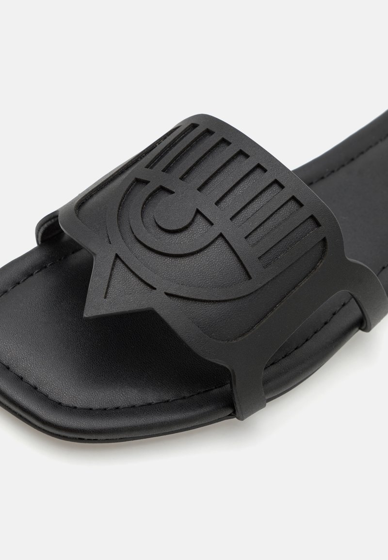 Schwarze offene Zehensandale mit einem breiten Riemen, der ein erhöhtes abstraktes Augendesign auf der Vorderseite zeigt.