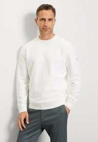 Weißer Pullover mit Rundhalsausschnitt und gerippten Bündchen, aus weichem Material gefertigt. Kombiniert mit dunkelgrauen Hosen, die ein dezentes Design aufweisen.
