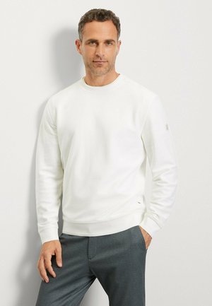 White sweatshirt with a crew neck and ribbed cuffs, made of soft material. Paired with dark grey trousers, featuring a subtle design.