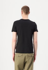 Black short-sleeve t-shirt made of soft cotton. Features a crew neck and minimal branding on the back. Worn with olive green pants.
