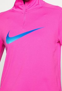 Maglietta sportiva a zip parziale in vivace tessuto rosa, con una finitura testurizzata e un logo Nike blu prominente sul fronte.