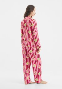 Conjunto de pijama rosa con rayas verticales y coloridos patrones de palomitas de maíz. Hecho de tela suave, incluye una parte superior con cuello y pantalones holgados.