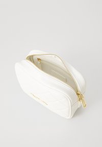 Weißes, gestepptes Kosmetiktäschchen mit goldenen Reißverschluss und Beschlägen, das eine gebogene Form und eine strukturierte Oberfläche aufweist. Innentasche sichtbar.