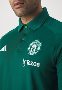Zelená polo triko s logem Manchester United, módou Adidas a logem Tezos. Vyrobeno z prodyšné tkaniny s texturovaným povrchem.