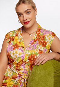 Blommig klänning med gröna, gula, orange och rosa mönster. Korta ärmar, knäppning fram, knytning i midjan. Mjuk tyg, avslappnad passform.
