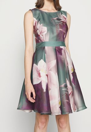 Robe sans manches en ligne A avec ceinture verte, tissu texturé et grand imprimé floral rose et blanc sur fond vert et violet.