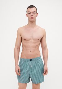 Boxers légers rayés turquoise avec taille élastique. Présente des lignes blanches verticales et une fermeture à bouton fonctionnelle à l'avant.