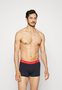 Morske bokserice z rdečim pasom z logotipom TOMMY HILFIGER. Mehka bombažna tkanina, prilegajoč dizajn in dolžina do sredine stegna.