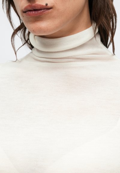 Πουλόβερ ζιβάγκο σε κρεμ απόχρωση, κατασκευασμένο από ελαφρύ, ημιδιαφανές ύφασμα, με ψηλό γιακά και λεπτή, λεία υφή.